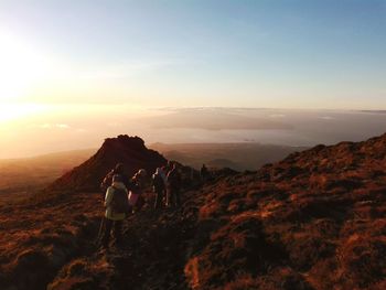 People walking on mountain against sky during sunset