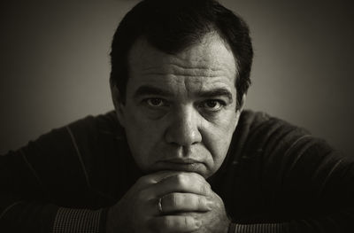 Portrait of serious mature man with hands on chin against gray background