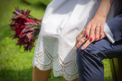 A detail of wedding rings on crossed hands of  sitting bride and a groom in a garden.