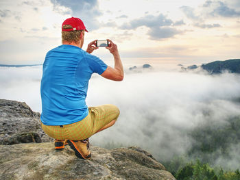 Man taking picture of amazing fall mountains on his phone in misty weather