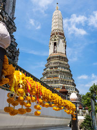 Wat arun temple in bangkok, thailand, with yellow flowers, phuang malai, and  blue sky with clouds.