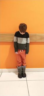 Full length of boy standing against orange wall on floor