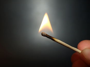 Close-up of hand holding illuminated candle against black background