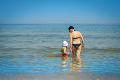 Rear view of mother and daughter in sea against sky