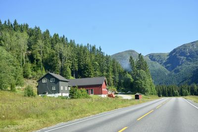 Road by trees and mountains against clear sky