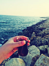 Midsection of person on rock by sea against clear sky