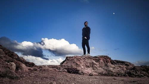 Low angle view of man standing on rock against blue sky