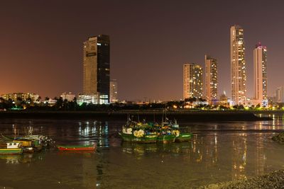 Illuminated buildings by river against sky at night