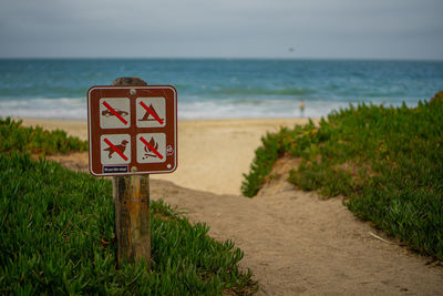 Warning sign on beach against sky