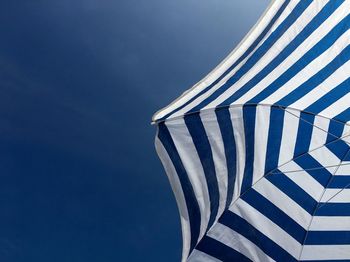 Low angle view of white and blue beach umbrella against blue sky