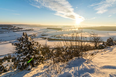 Snow covered land against sky during sunset