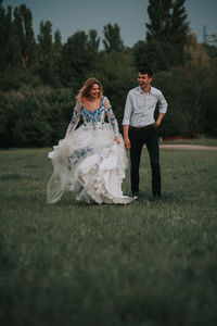 Cheerful couple walking on grass against sky