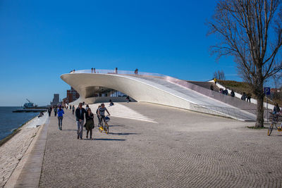 People walking on road against clear blue sky