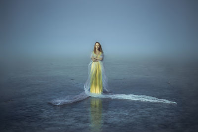 Beautiful woman standing on frozen lake rink against foggy weather