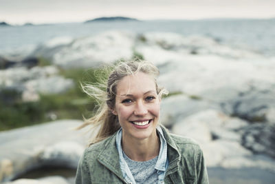 Portrait of happy young woman on rock by sea