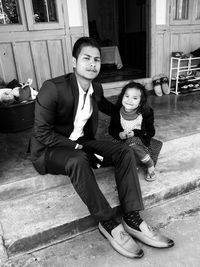 Portrait of smiling man and girl sitting outside house