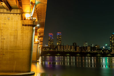 Illuminated buildings by river against sky at night