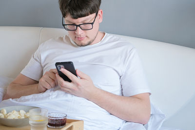 Young man using mobile phone while sitting on bed at home
