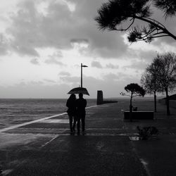 Rear view of silhouette couple walking on pier against sky during monsoon