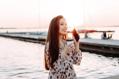 Young woman using smart phone by sea against sky