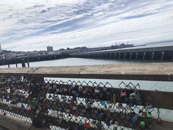 Padlocks on bridge over river against sky