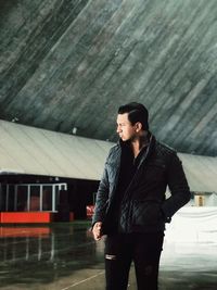 Young man looking away while standing against wall