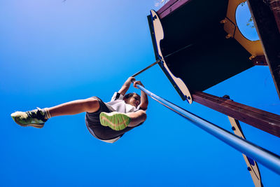 Low angle view of boy hanging on pole against clear blue sky