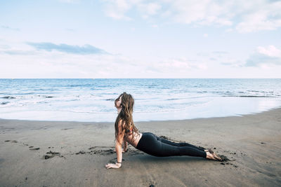 Full length side view of woman stretching while exercising on shore at beach
