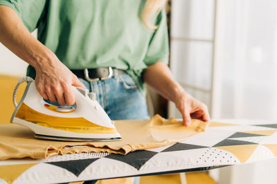 Close-up of an unrecognizable woman ironing clothes with steam on an ironing board.