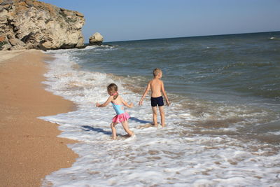 Children walking on beach against clear sky