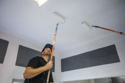 Painter uses roller to paint ceiling white.