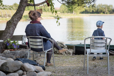 Rear view of mother and son sitting on chairs by lake