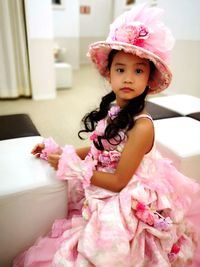 Portrait of cute girl wearing pink dress sitting at home