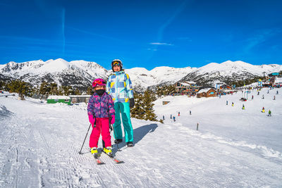 Mother and daughter with ski resort, snow capped mountains and forest in background, andorra