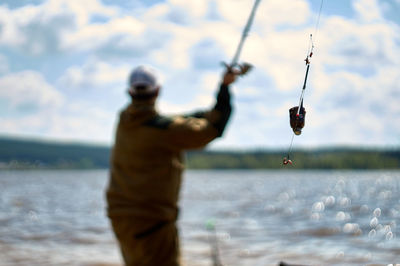 Man fishing by sea against sky