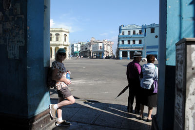 Side view of mature woman leaning on wall at sidewalk in city