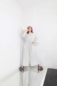 Full length fashion catalog style portrait of woman in jumpsuit standing on mirror over white wall