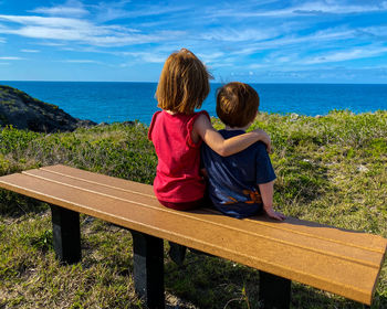 Rear view of woman sitting on bench looking at sea against sky