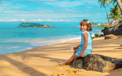 Portrait of smiling girl sitting on rock at beach