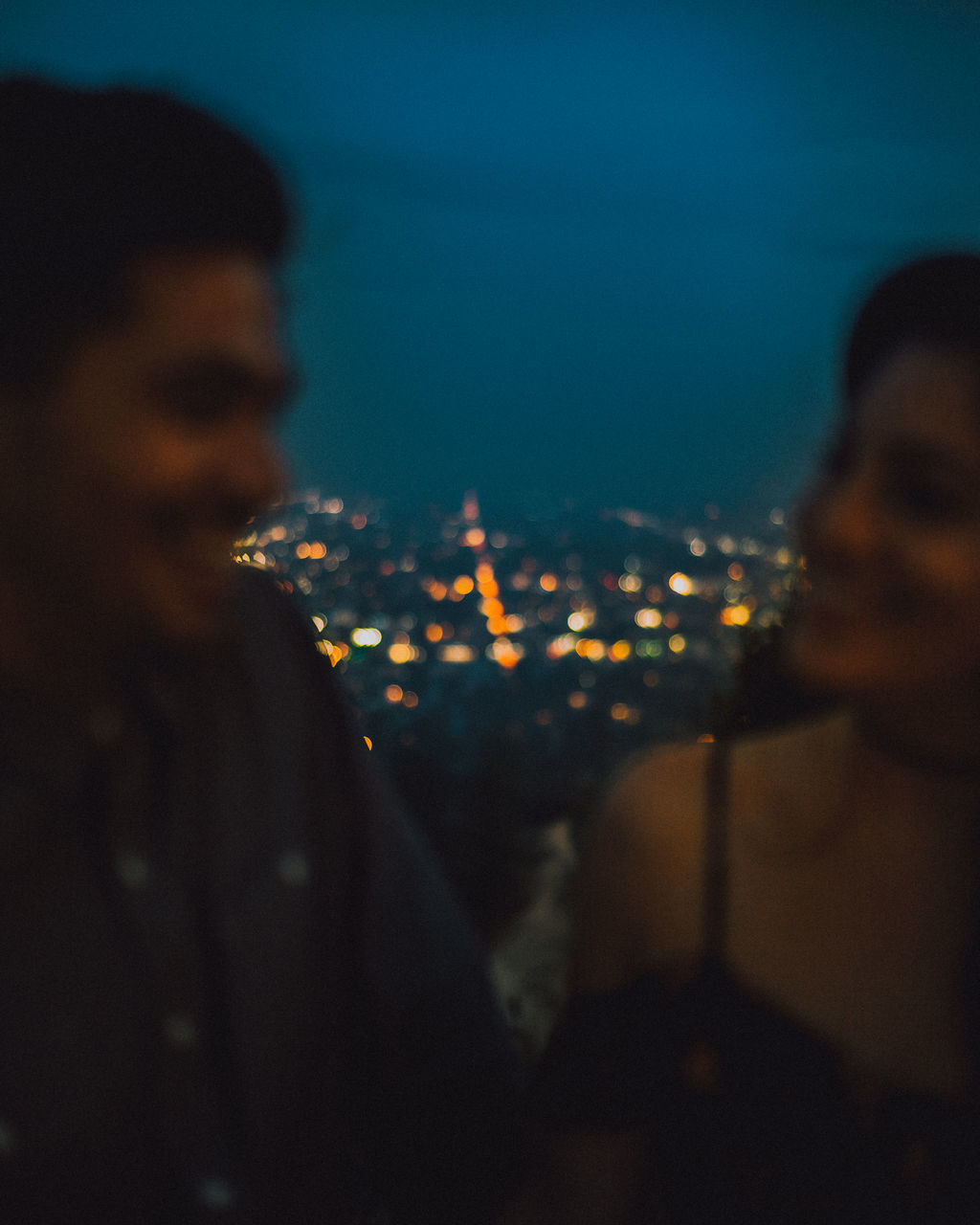 PORTRAIT OF MAN LOOKING AT ILLUMINATED CITYSCAPE AGAINST SKY