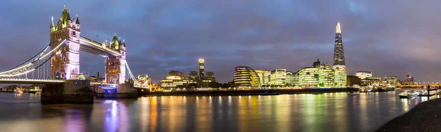 Illuminated city by river against sky at night