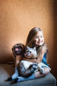 Portrait of happy girl with pets sitting on ottoman at home