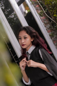 Portrait of a beautiful young woman standing against window