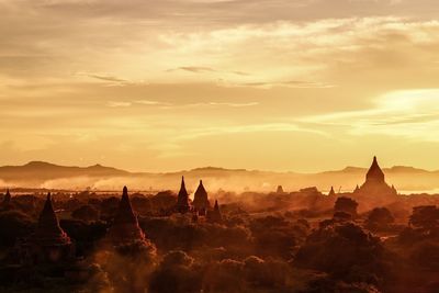 Pagodas and trees against sky during sunset