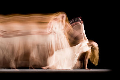 Blurred motion of woman dancing against black background