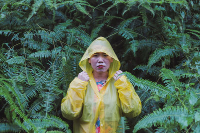 Portrait of woman in raincoat standing against plants