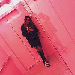 Full length portrait of woman standing against pink wall