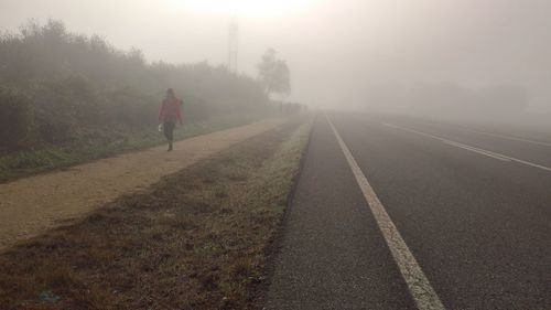 Woman walking on footpath by road in foggy weather
