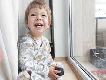 Portrait of cute girl sitting on window at home