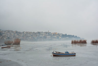 Winter scene with boats in frozen ice and town of kastoria covered with snow